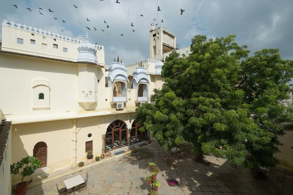 Fort courtyard seen from a gallery, painted white balconies and a large tree, birds overhead