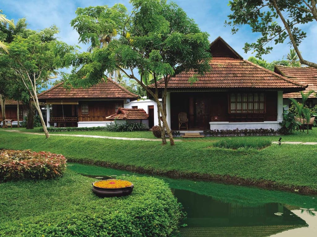 Heritage Lake View Villas with carved gables and tiled roofs beside a lily pond and coconut palms, Kumarakom Lake Resort, Kumarakom
