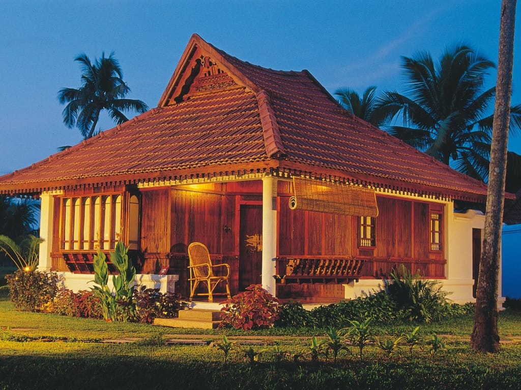 Heritage Villa in traditional Kerala wood and tile lit at dusk with cane chair on the verandah, Kumarakom Lake Resort, Kumarakom