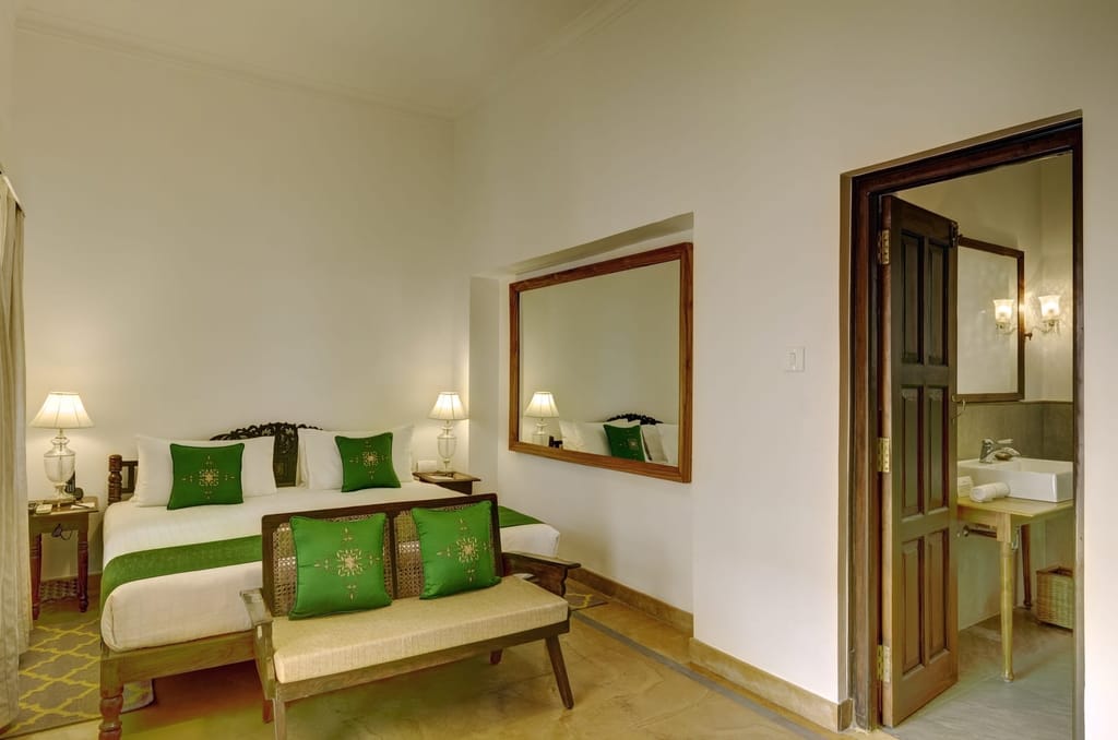 Awadh Room with carved dark-wood bed, green cushions and a bench seat, Saraca Hotel Lucknow, Lucknow