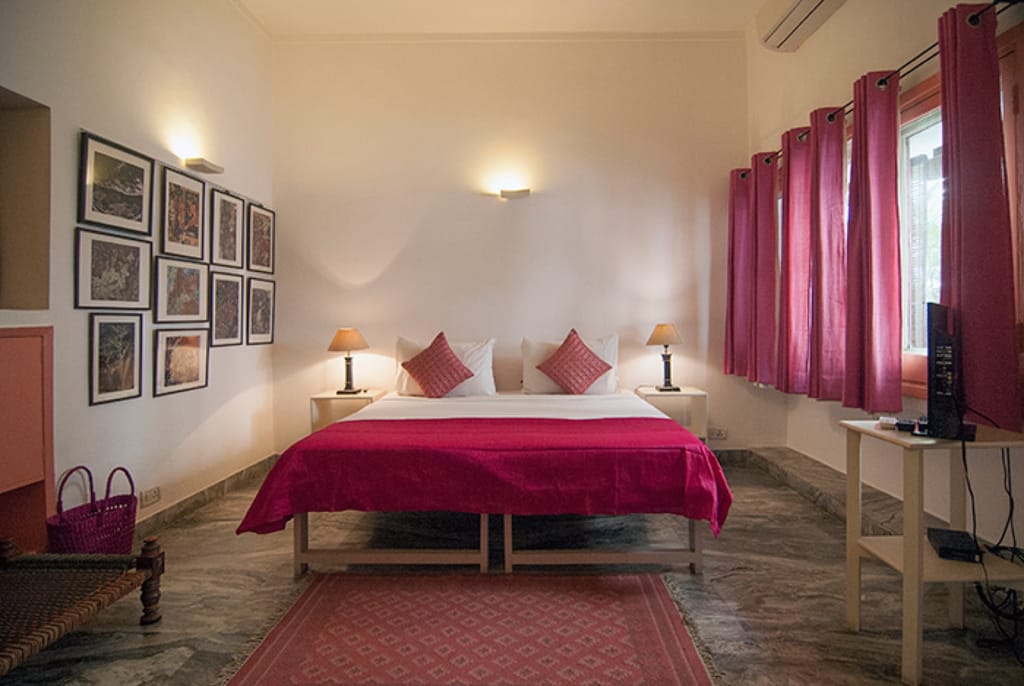 Ajanta room with framed cave-painting prints and crimson bedspread, Haveli Hauz Khas, New Delhi