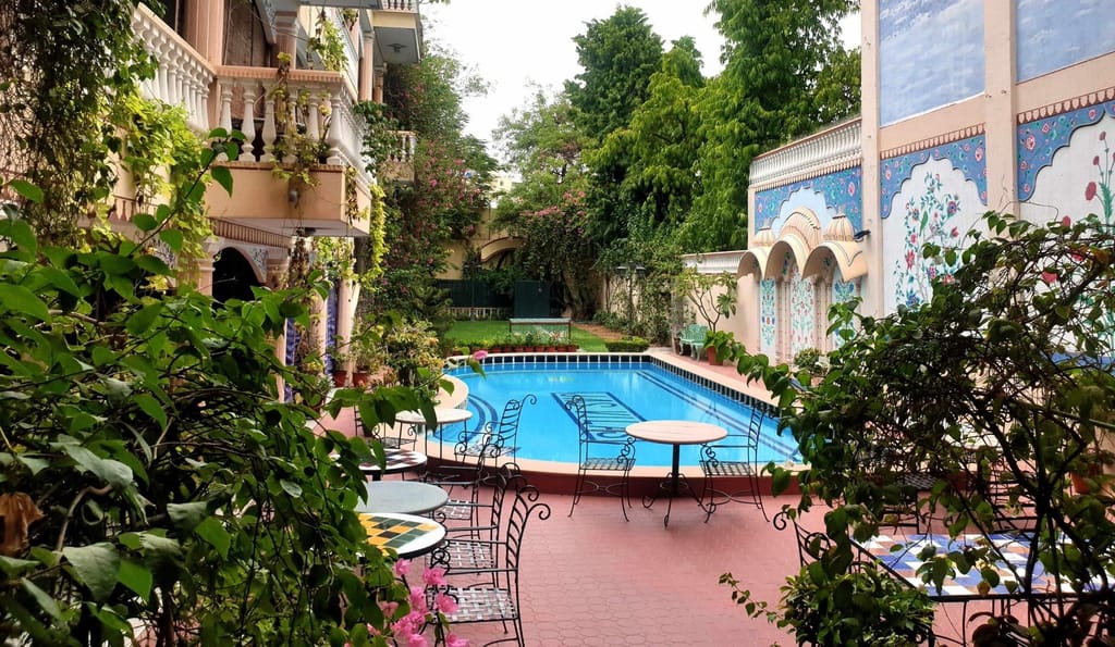 Pool and painted courtyard wall seen through the garden, Jas Vilas, Jaipur