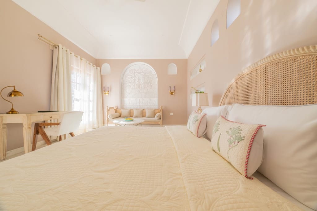 Pink-plastered bedroom with arched cane headboard and Krishna wall relief, Niravi, Jaipur
