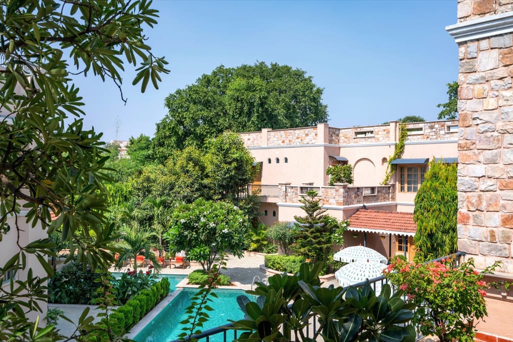 Stone-clad Estate wing and tiled pool seen through frangipani and palms, Niravi, Jaipur