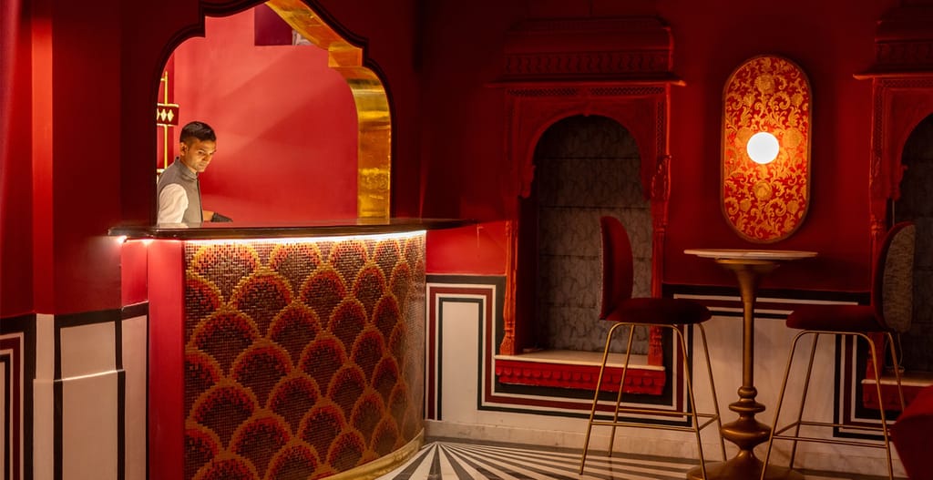 Red-lacquered courtyard bar with gold mosaic counter and carved jharokha niches, Padmaa, Jaipur