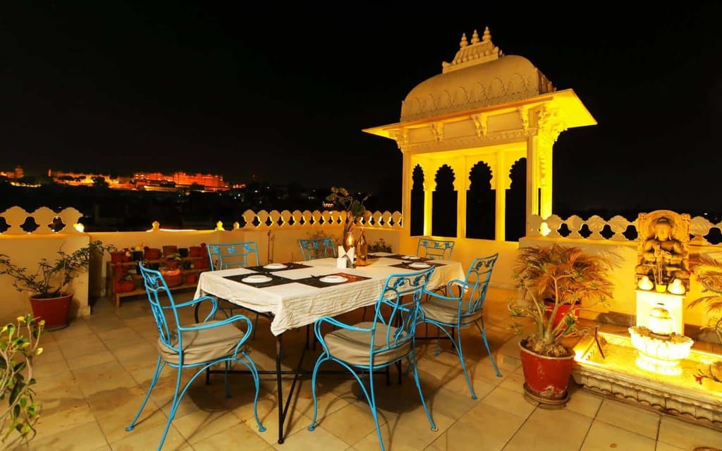 Rooftop restaurant table at night with lit chhatri and fort view