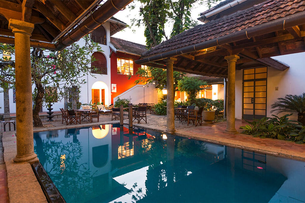 Courtyard pool of The Malabar House in daylight, ringed by stone columns, tiled roofs and garden