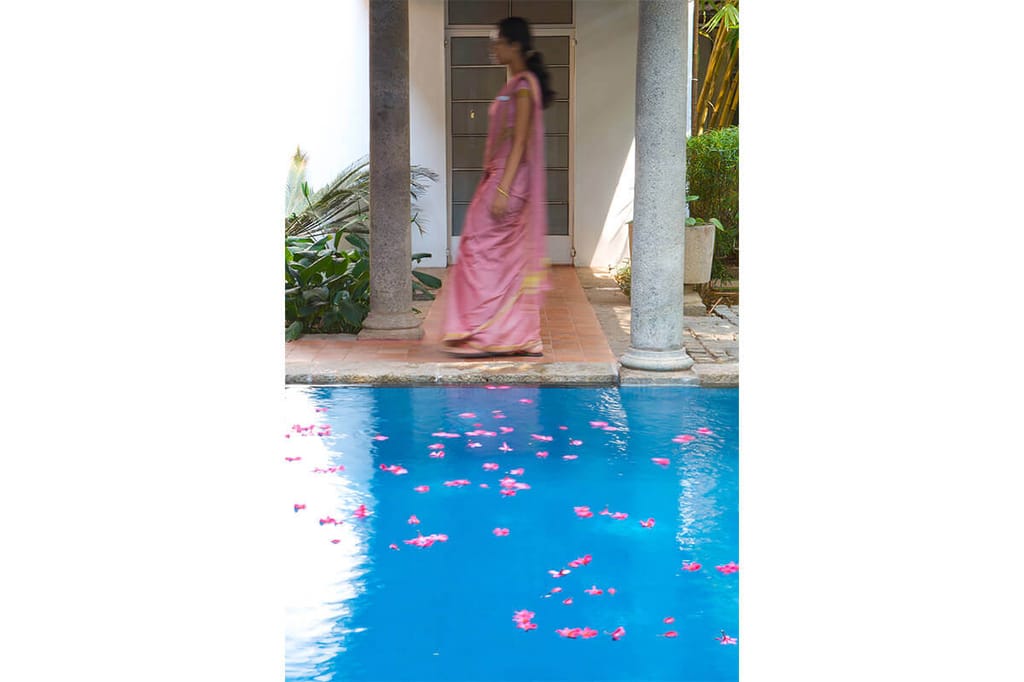 Flower petals floating on the courtyard pool at The Malabar House beside a carved wooden pillar