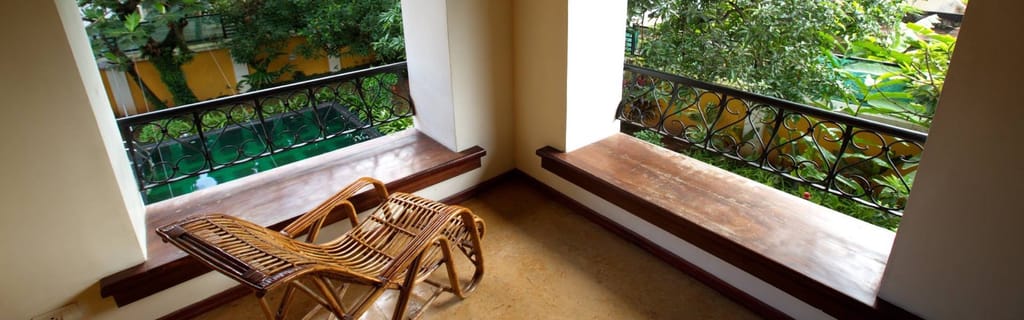 Tea Bungalow, Fort Kochi: covered balcony with cane recliner and built-in timber bench looking over the garden and pool