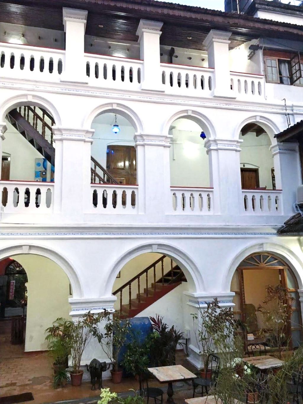 Arched arcades and the staircase of The Old Courtyard Hotel, Fort Kochi, with potted plants at ground level