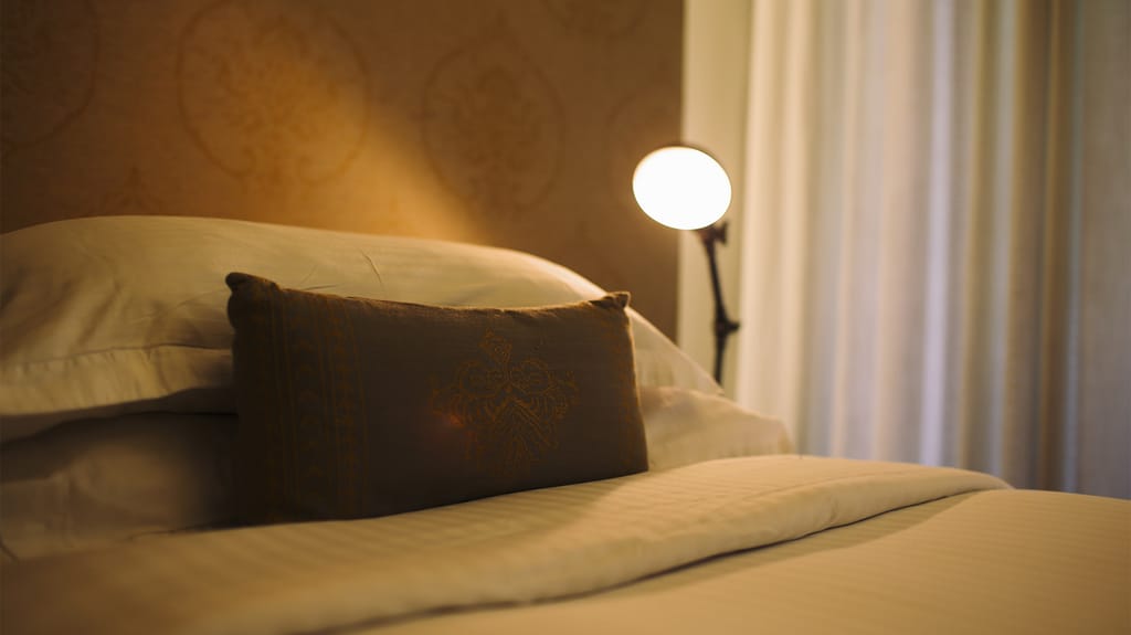 Bed detail with embroidered cushion and reading lamp in a Bastion Room