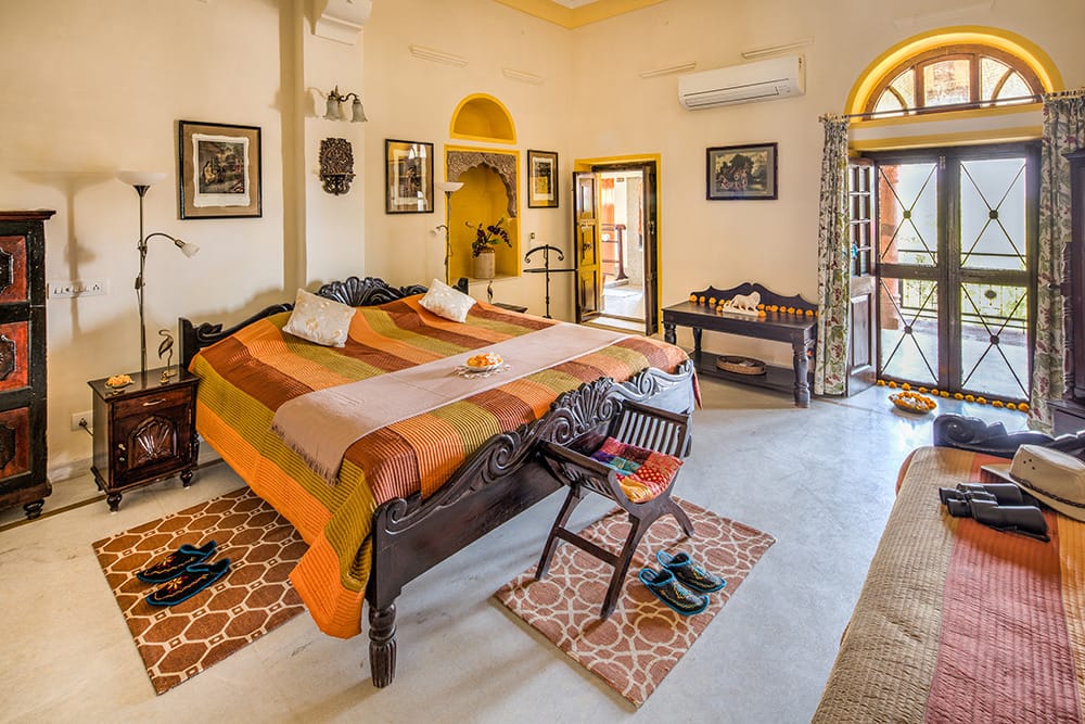 Suite bedroom with a carved wooden bed, framed photographs on the walls and doors open to a terrace