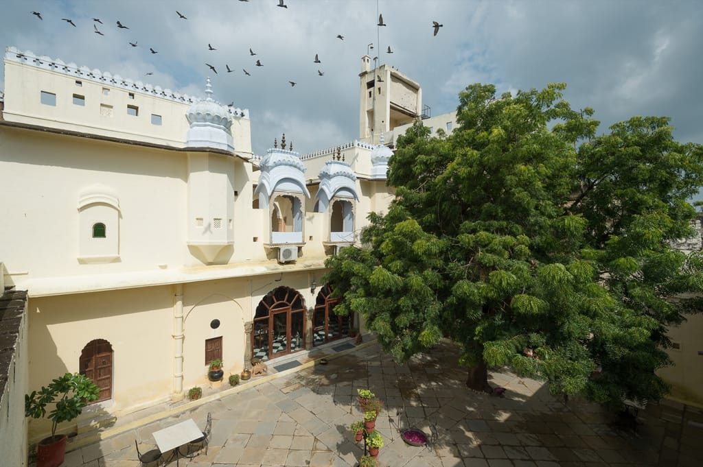 Fort courtyard seen from a gallery, painted white balconies and a large tree, birds overhead
