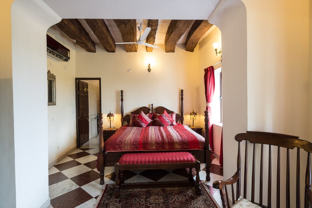 Bedroom with a four poster bed under exposed timber beams and a chequerboard marble floor