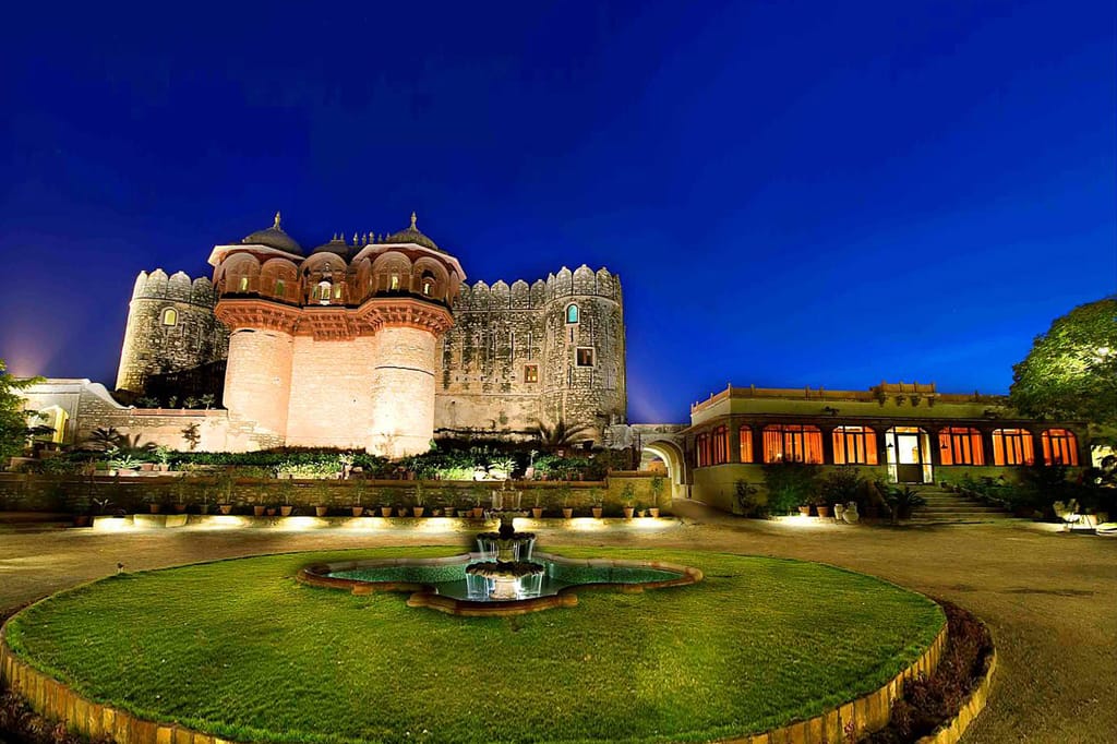 Floodlit fort above a lawn and fountain