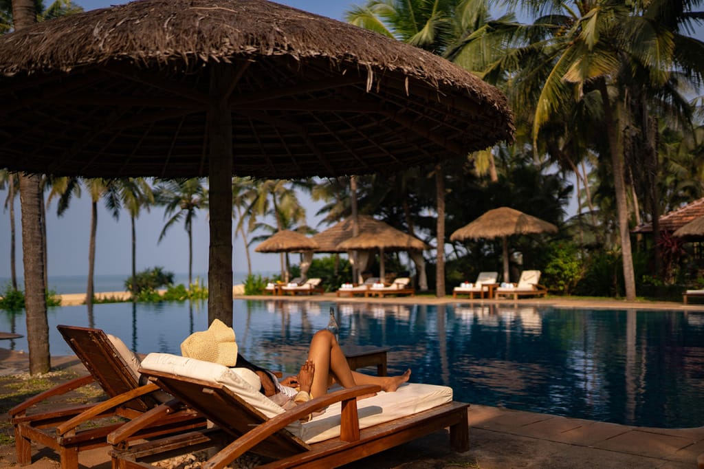 Infinity pool with thatched parasols and loungers, the sea beyond the palms