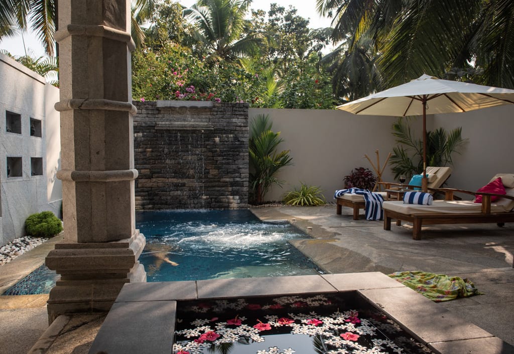 Private plunge pool with a stone water wall, loungers and a parasol
