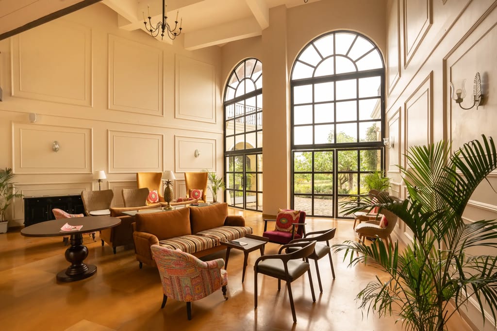 Double-height lounge with tall arched windows, panelled walls and mid-century armchairs