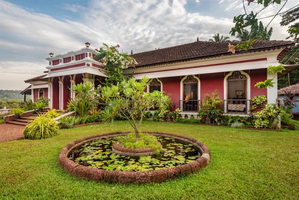Front facade: deep red Portuguese house with whitewashed arches, tiled roof and circular lily pond on the lawn. Extracted from the hotel's official e-brochure PDF, page 3.