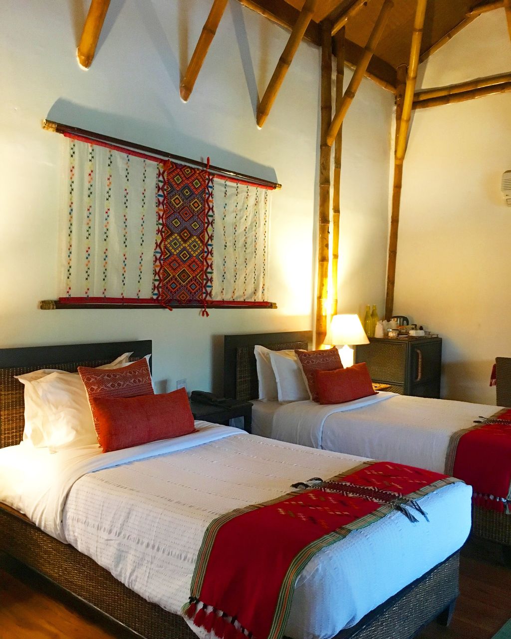 Twin beds with red throws and a woven wall hanging