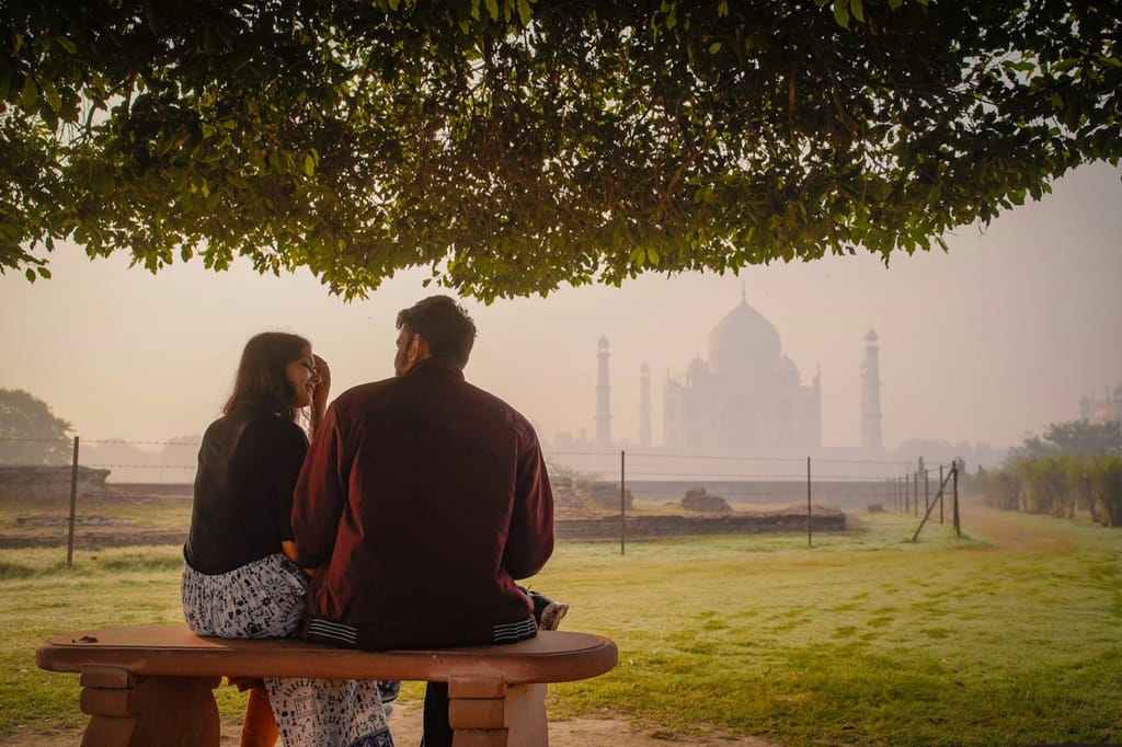A couple on a bench looking out to the Taj Mahal in the morning haze