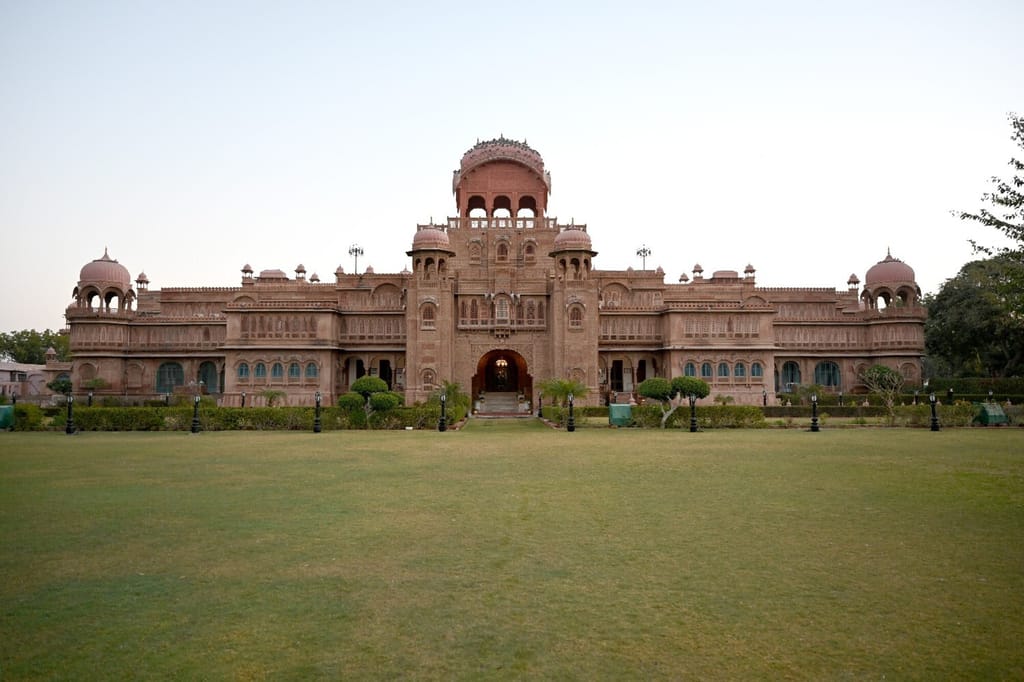 Red sandstone palace facade with domes and lawns at dusk