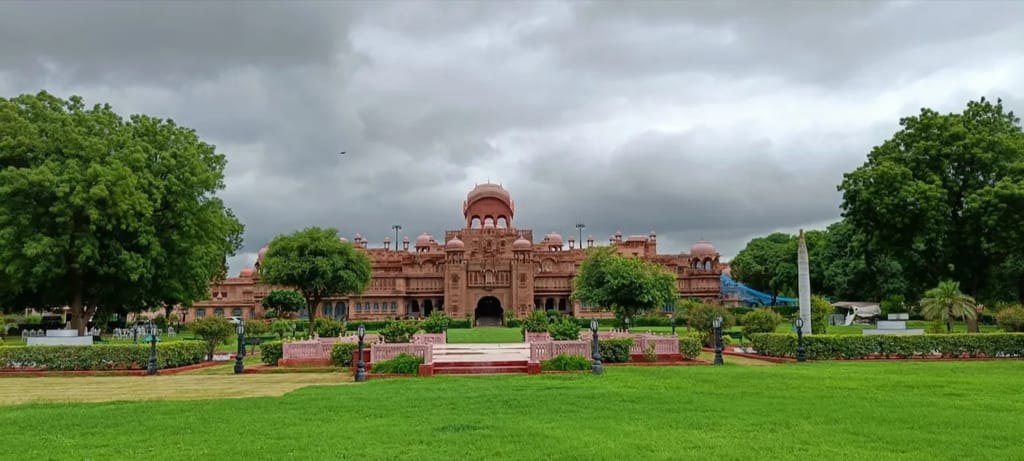 The red-sandstone facade of The Laxmi Niwas Palace, Bikaner, its domes and cupolas rising over formal lawns