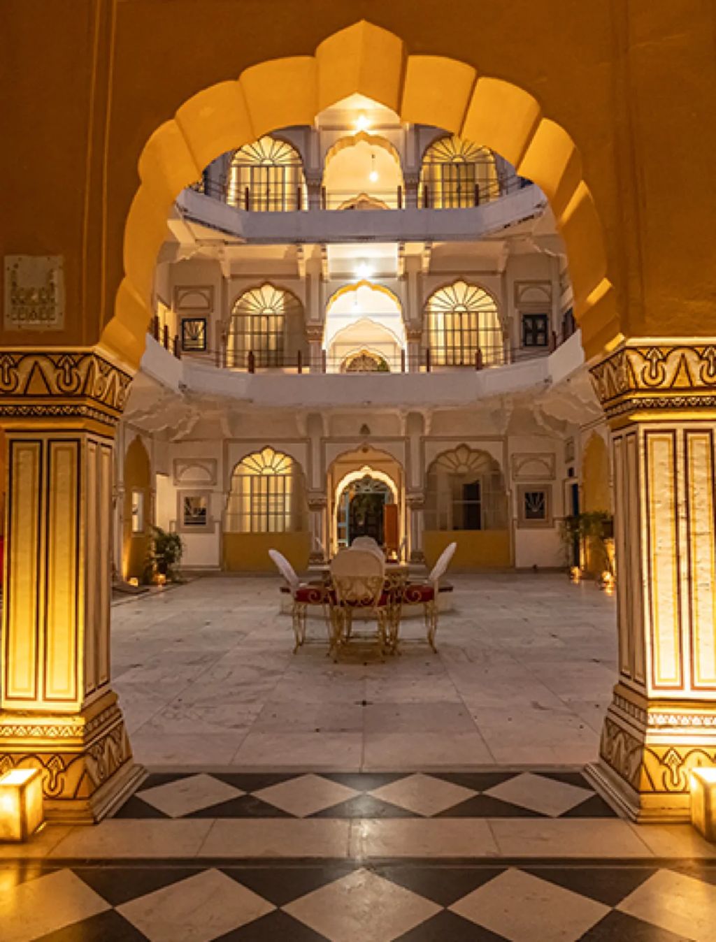 A lamplit inner courtyard of Hotel Diggi Palace seen through a scalloped arch at night, Jaipur