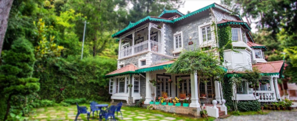 Grey stone villa with green trim roofs and a lawn
