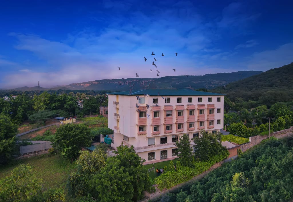 Aerial view of the resort building against Aravalli hills with birds overhead