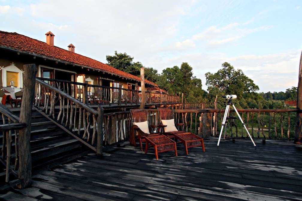 Main lodge building with red-tiled roof, timber-railed deck, safari chairs and a telescope at Samode Safari Lodge, Bandhavgarh