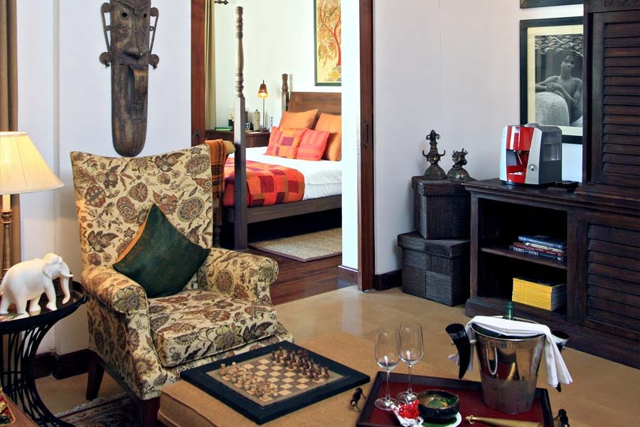Villa sitting room with floral armchair, chess board and a view through to the four-poster bed at Samode Safari Lodge, Bandhavgarh
