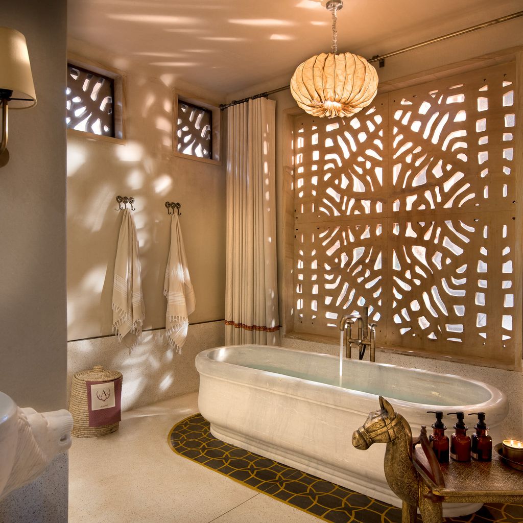 Kothi bathroom with freestanding stone bath beneath a carved jali window at Aramness, Sasan Gir