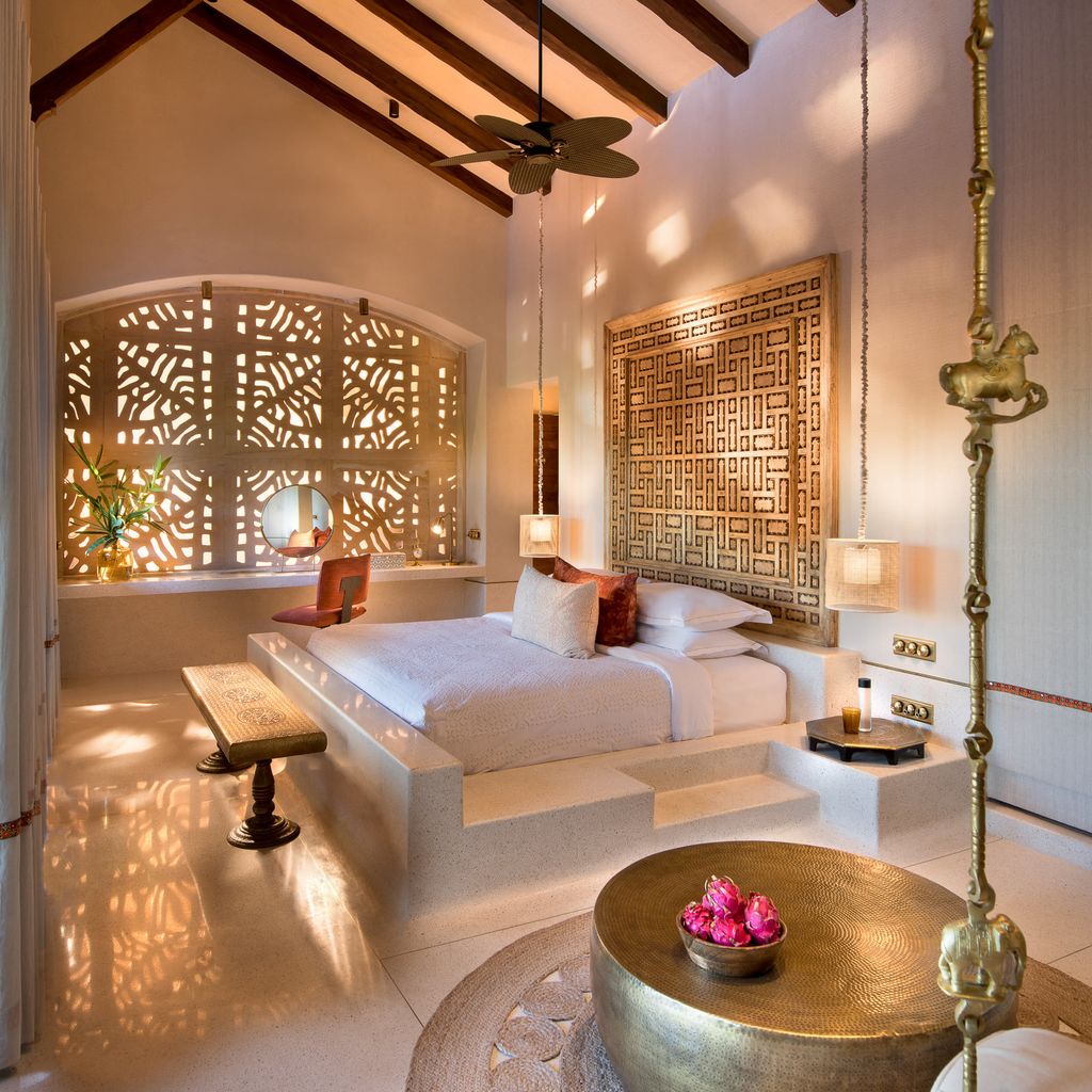Kothi bedroom with platform bed, carved wooden headboard panel, brass swing and backlit jali screen at Aramness, Sasan Gir