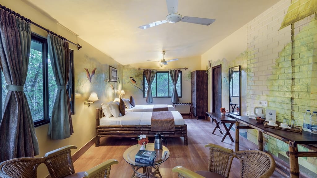 Executive Room — twin bamboo beds, cane armchairs and bird murals on the painted brick wall at Sundarban Tiger Camp, Sundarbans