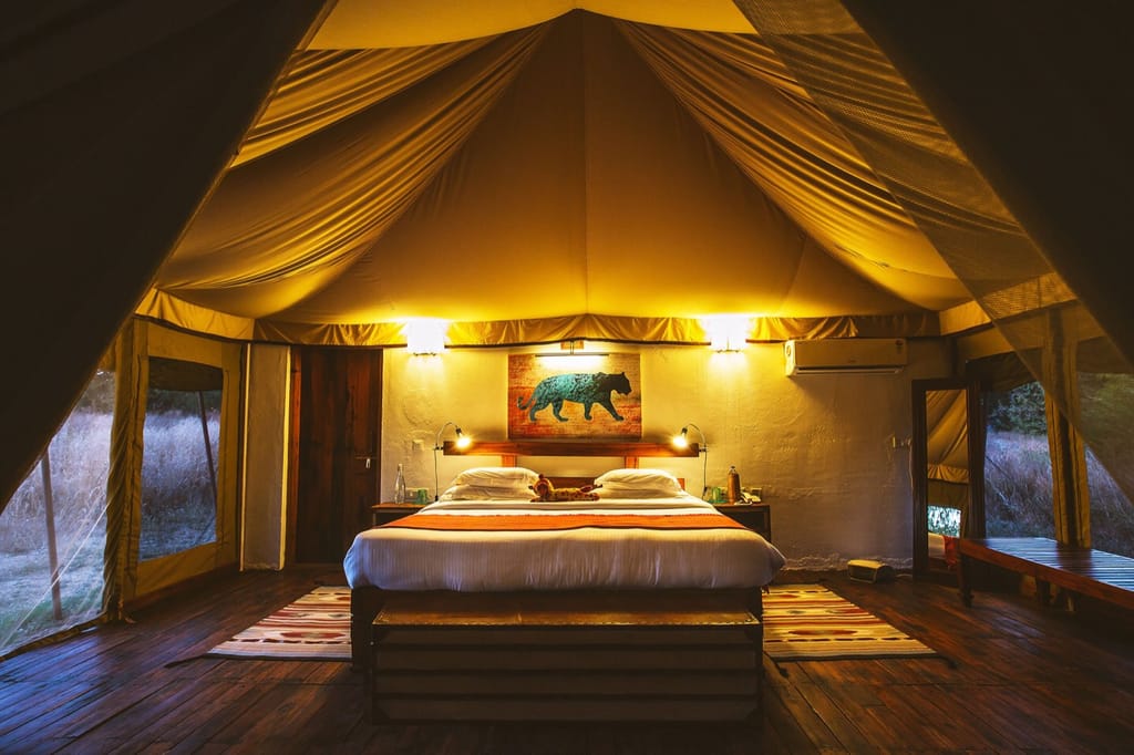 Luxury Tent — king bed under the lamplit canvas canopy with tiger artwork above the headboard at Jamtara Wilderness Camp, Pench