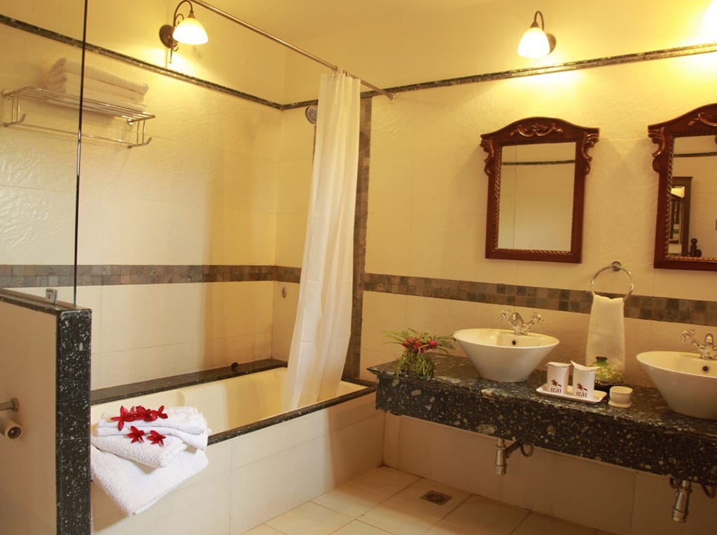 Bathroom with bathtub, twin basins on a granite counter and carved wooden mirrors at Irai Safari Retreat, Tadoba