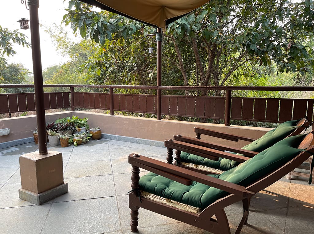 Terrace with cushioned wooden loungers under a canvas canopy overlooking greenery at Irai Safari Retreat, Tadoba