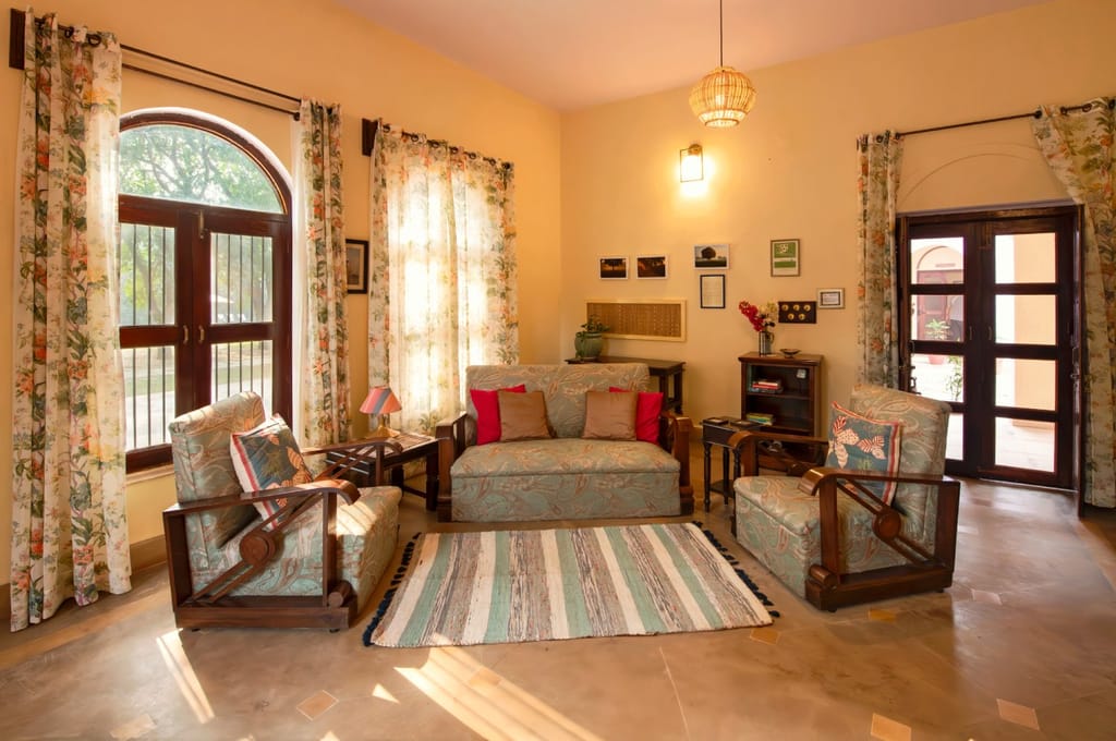 Sitting room with paisley upholstered sofa and armchairs, floral curtains and arched windows at Mela Kothi – Chambal Safari Lodge, Chambal