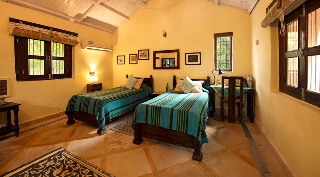 Twin-bedded room with green striped covers under a whitewashed sloping roof at Mela Kothi – Chambal Safari Lodge, Chambal