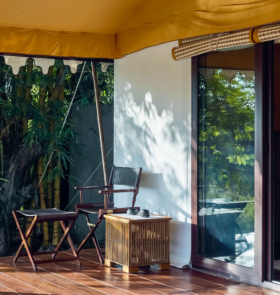 Tented Suite — campaign chair and cane table on the verandah beside bamboo at Bagh Villas, Kanha