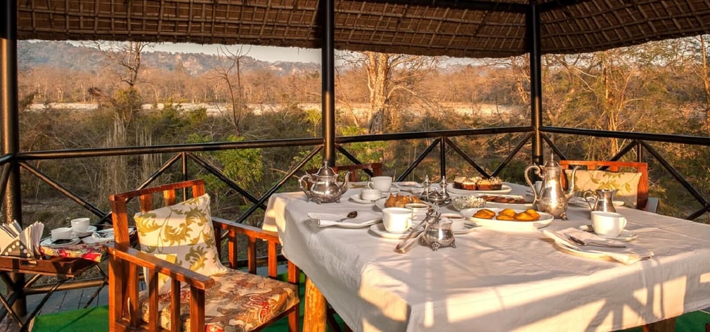 Breakfast with silver teapots on a covered machan deck overlooking the riverbed and forest at Jim's Jungle Retreat, Corbett