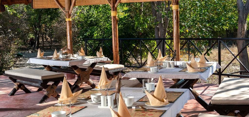 Open-air dining pavilion with bamboo pillars and tables laid for breakfast at Jim's Jungle Retreat, Corbett