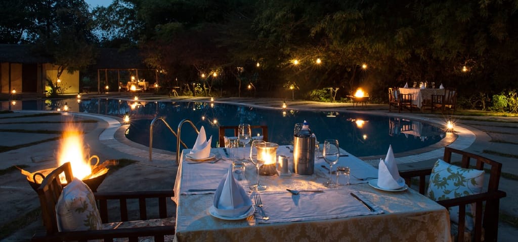 Candlelit dinner table beside the swimming pool at dusk with fire braziers at Jim's Jungle Retreat, Corbett