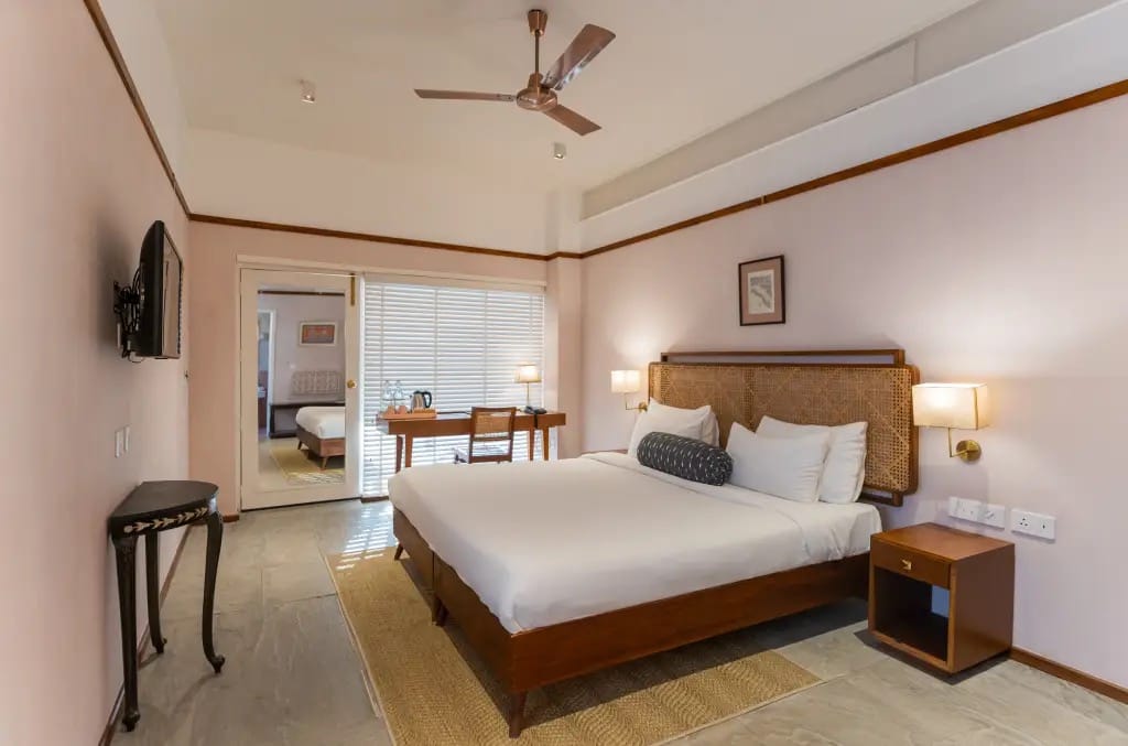 Angirasa bedroom with cane headboard, writing desk and sliding door to the connecting room at Amrit Bhawan, Haridwar