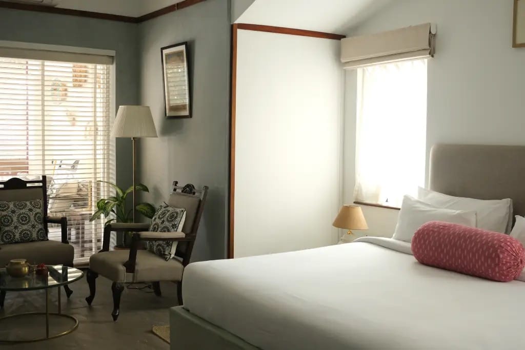 Atri bedroom with pink bolster cushion, wooden window seat and en-suite bathroom at Amrit Bhawan, Haridwar