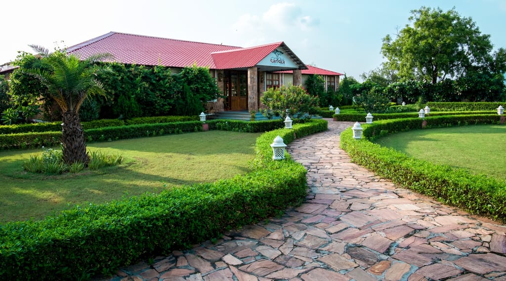 Red-roofed lodge entrance with stone pathway, clipped hedges and lantern-lined lawns at Sariska Safari Lodge, Sariska