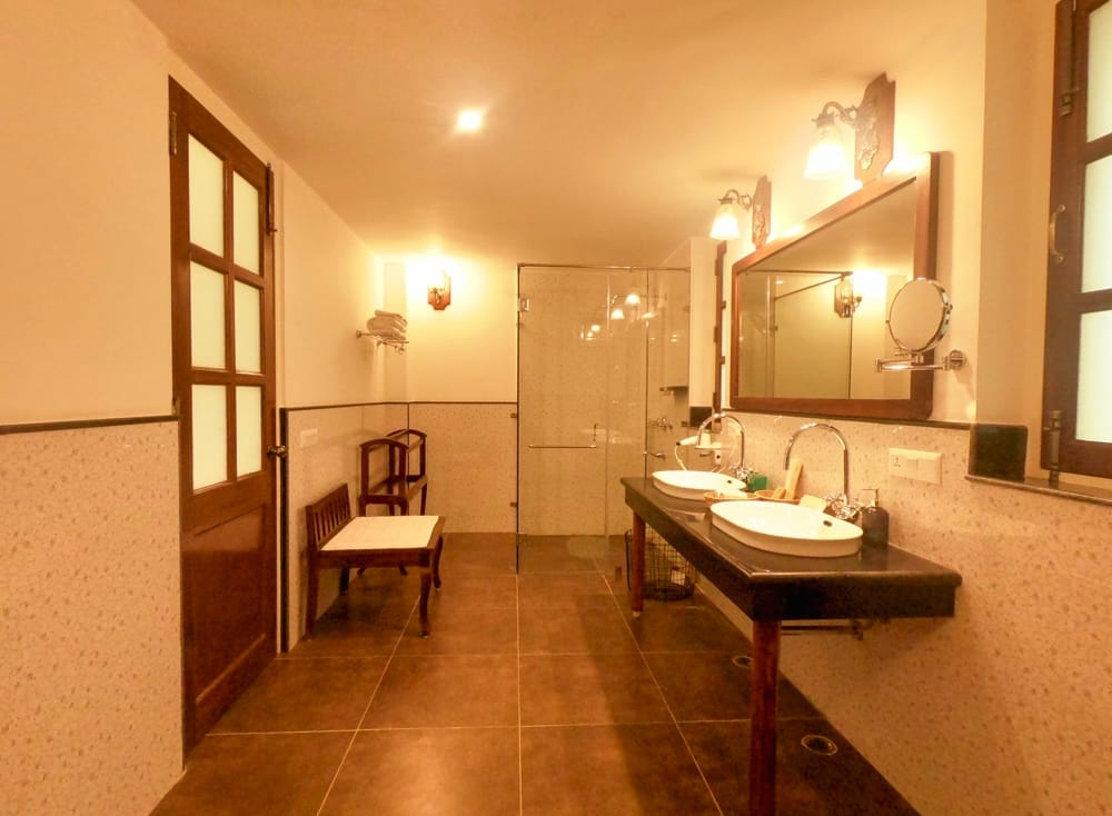 Luxury Cottage bathroom with twin basins, glass shower and seating bench at Sariska Safari Lodge, Sariska