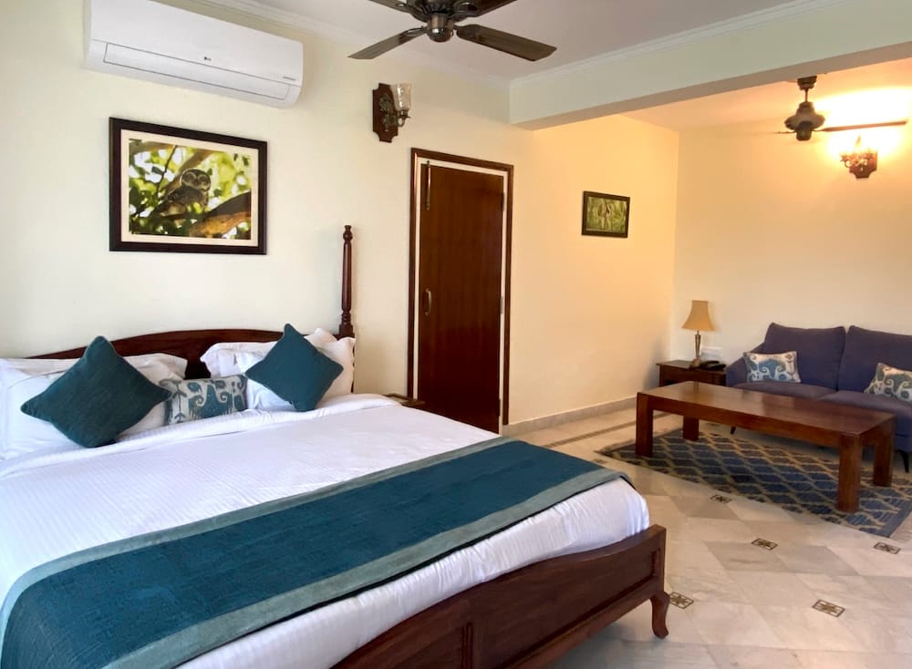 Luxury Cottage bedroom with king bed, teal cushions, owl photograph and sitting area at Sariska Safari Lodge, Sariska