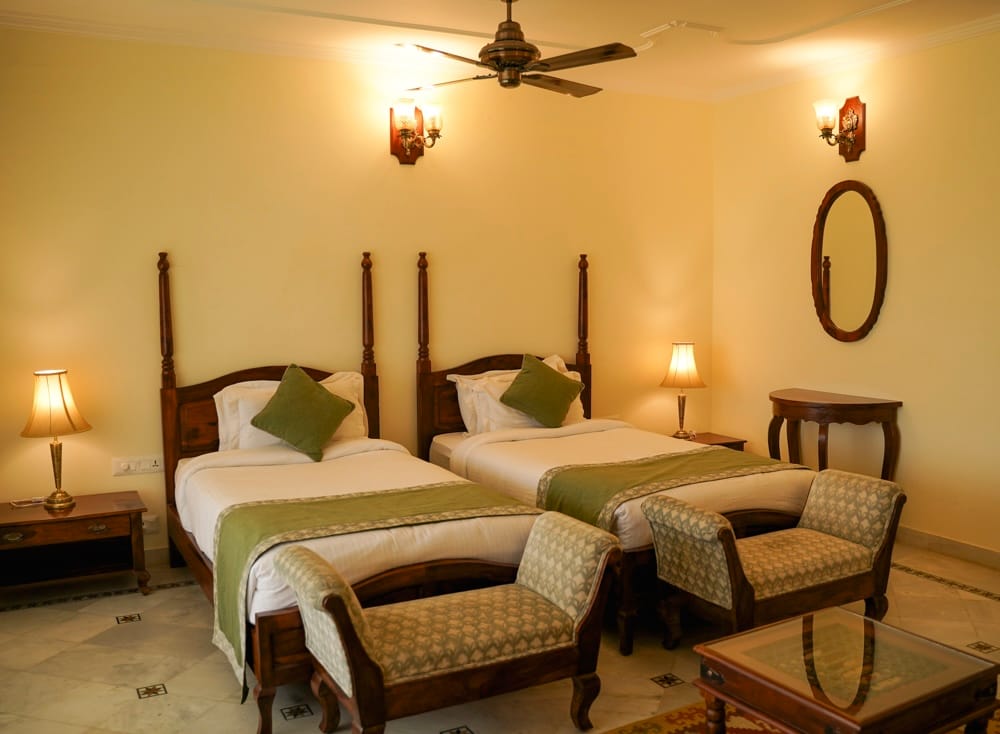 Luxury Cottage twin-bedded room with four-poster beds, green throws and upholstered benches at Sariska Safari Lodge, Sariska